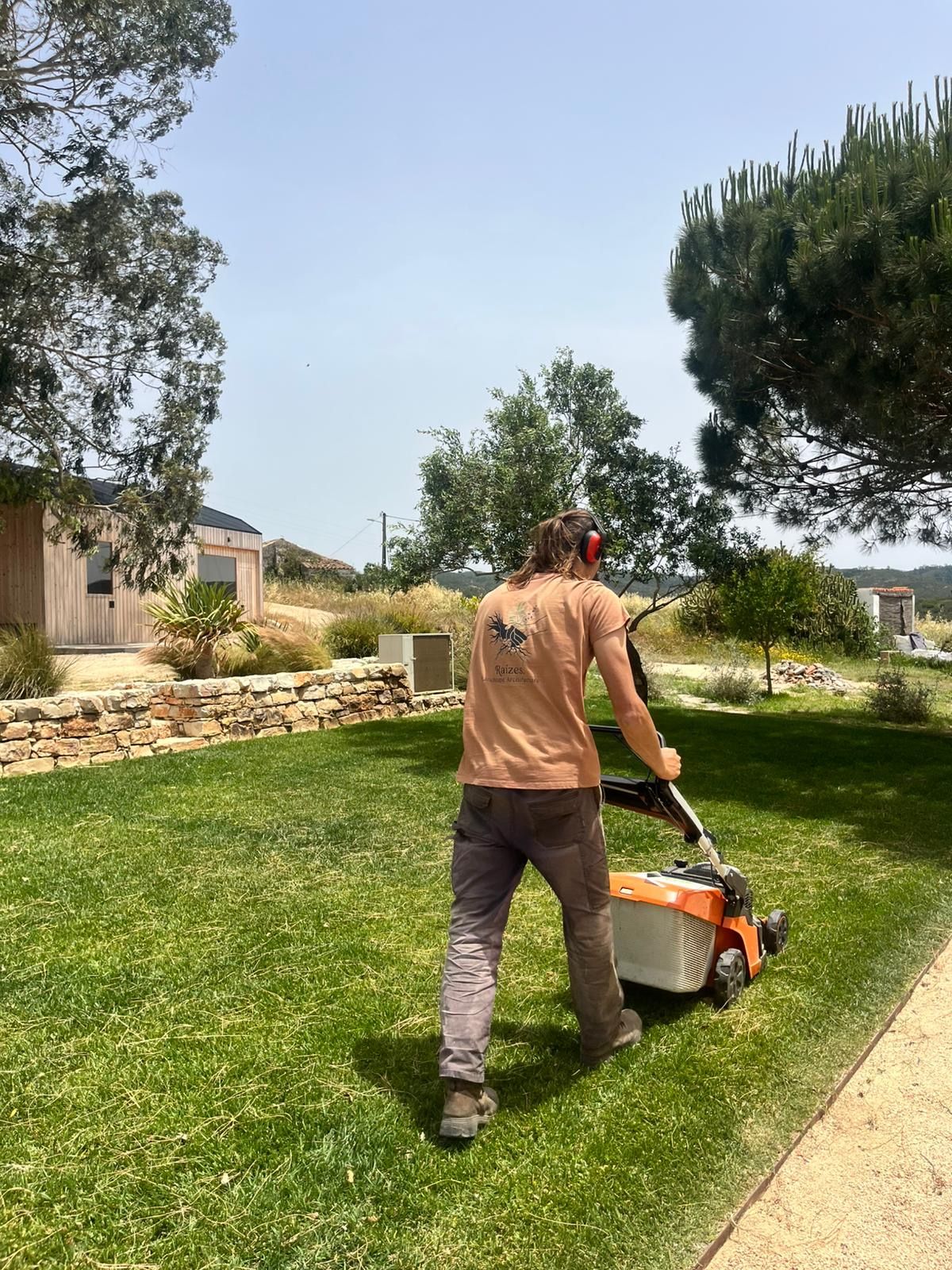 Crew member mowing a lawn by a dry stone wall