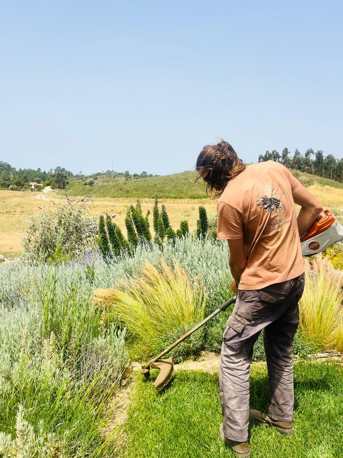 Crew member trimming grass edges in a Raízes t-shirt